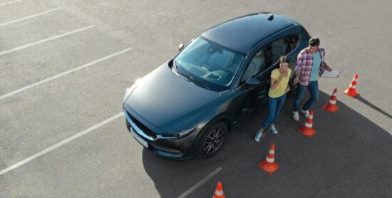 Instructor with clipboard near car and his student outdoors, above view. Driving school exam